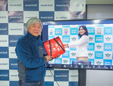 山形県遊佐町との浮くっしょん贈呈式の写真。遊佐町長はオンラインで出席し、大型モニターに映っています。