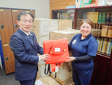 寄贈された浮くっしょんが入った段ボールと、その前で浮くっしょんを持つ男性と女性。
