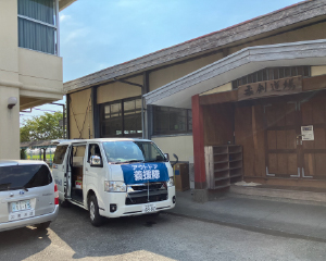 中学校の柔剣道場の前に支援物資を載せた車が停まっています。