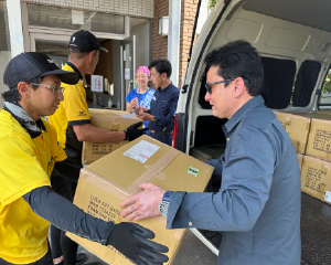 野口さんがボランティアスタッフから段ボールを受け取り、車に積み込んでいます。