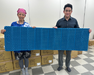 野口さんと女性がマットを広げて持っています。